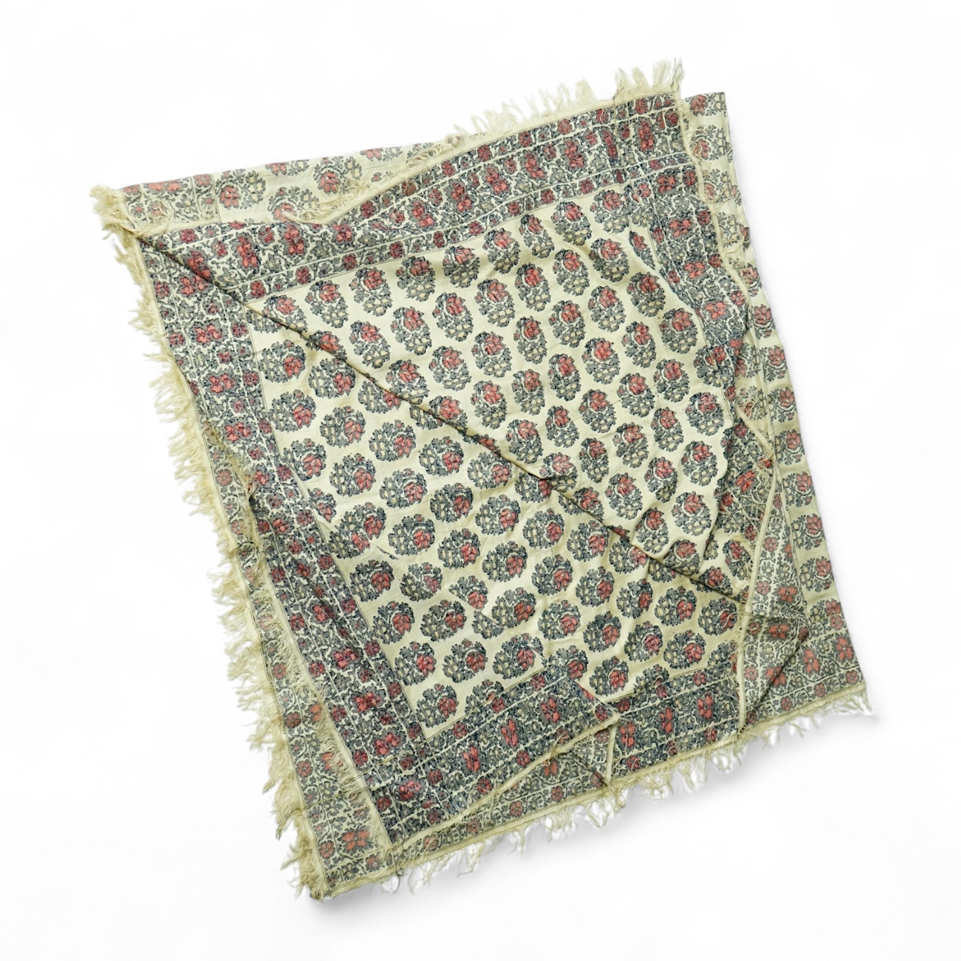 A 19th century silk woven shawl. Woven with a cream silk ground, with indigo, red and yellow, floral stylistic Buta motifs and bordered with three rows of a similar floral vining pattern. The edges fringed. 148cm x 152cm